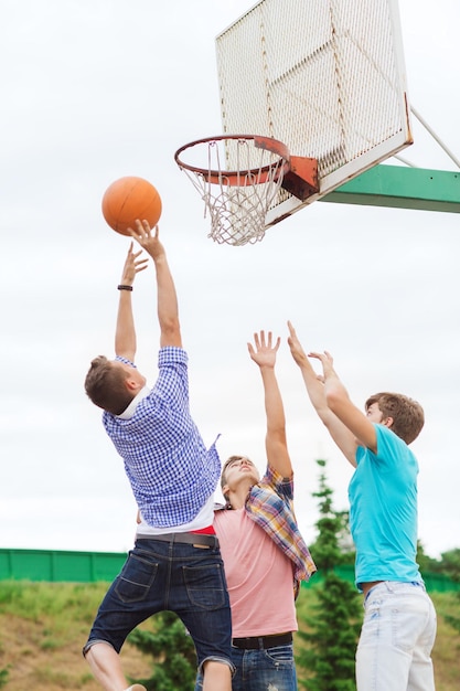férias de verão, feriados, jogos e conceito de amizade - grupo de adolescentes jogando basquete ao ar livre