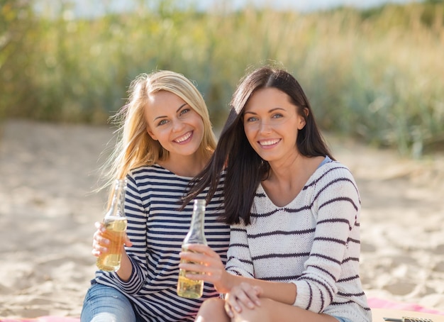Férias de verão, férias, celebração e conceito de pessoas - adolescentes felizes ou mulheres jovens bebendo cerveja ou limonada na praia