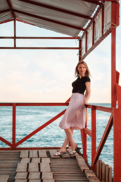 Férias de verão linda senhora em um vestido posando no cais à noite do mar