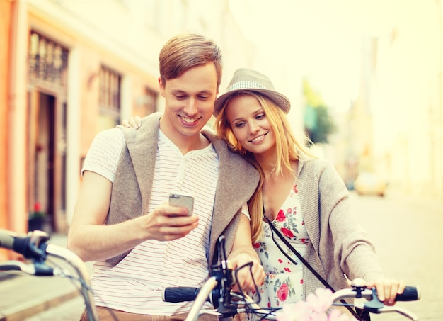 férias de verão, navegação, gps e conceito de namoro - casal com bicicletas e smartphone na cidade
