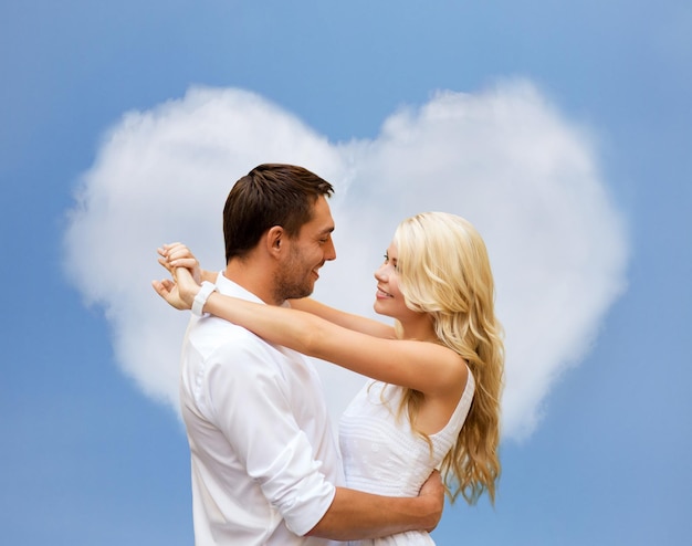 férias de verão, pessoas, amor e conceito de namoro - casal feliz abraçando sobre nuvem em forma de coração e fundo de céu azul
