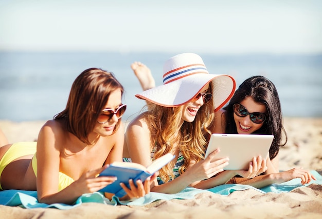 férias de verão, tecnologia e conceito de internet - garotas de biquíni tomando sol na praia com tablet pc