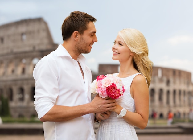 férias de verão, viagens, turismo, pessoas e conceito de namoro - casal feliz com um monte de flores sobre o fundo do coliseu