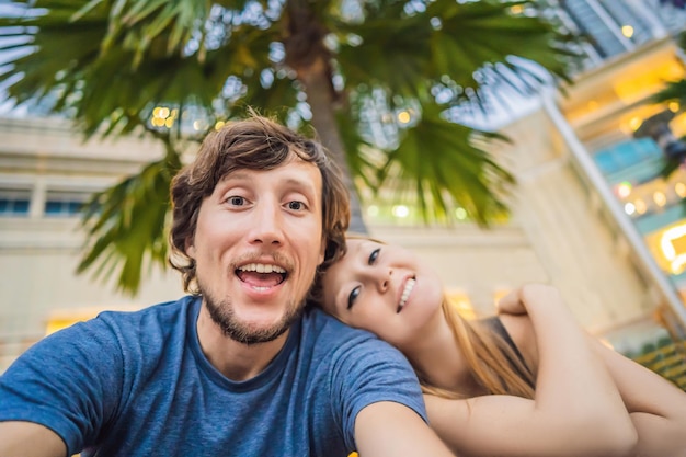 Férias de viagem e conceito de férias Casal feliz se divertindo tomando selfie sobre o parque com fundo de palmeiras e arranha-céus