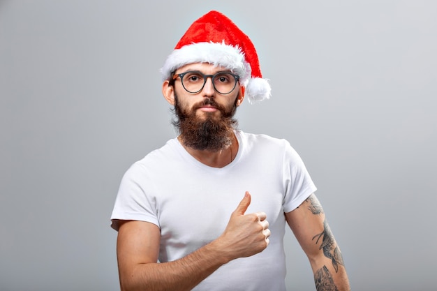 Férias e conceito de pessoas - retrato de um homem bonito e brutal com chapéu de Natal. Mais cinza