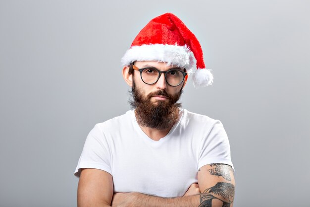 Férias e conceito de pessoas - retrato de um homem bonito e brutal com chapéu de Natal. Sobre um fundo cinza.