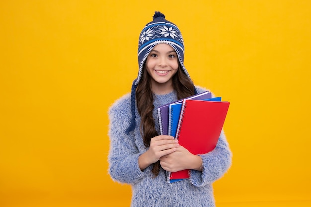 Férias escolares de inverno De volta à escola Aluna adolescente com chapéu quente e suéter em fundo amarelo estúdio isolado Escola de inverno