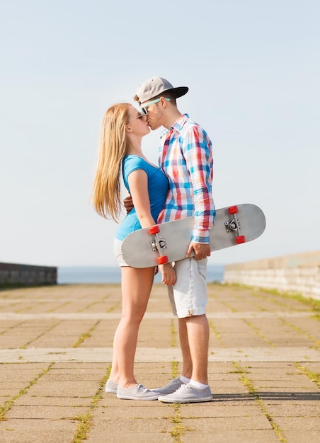 férias, férias, amor e conceito de amizade - casal sorridente com skate beijando ao ar livre