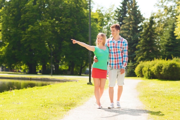 férias, férias, conceito de amor e amizade - casal sorridente caminhando e apontando o dedo no parque