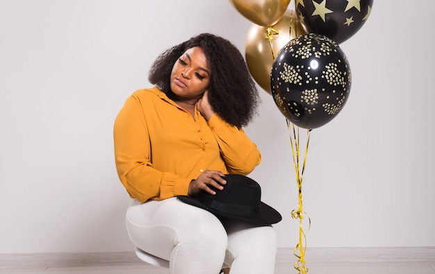 Férias, festa de aniversário e conceito divertido - retrato de uma jovem mulher afro-americana sorridente, elegante em um fundo branco segurando balões.