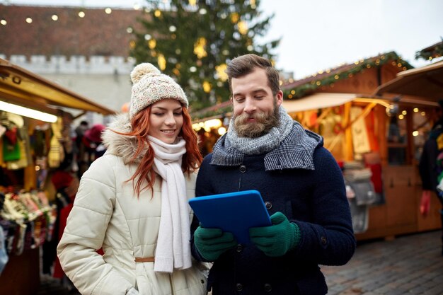 férias, inverno, natal, tecnologia e conceito de pessoas - casal feliz de turistas em roupas quentes com computador tablet pc andando na cidade velha