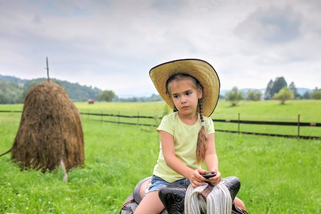 Férias locais, fique seguro, fique em casa. Menina com chapéu de cowboy brincando no faroeste na fazenda entre montanhas, feliz verão no campo, infância e sonhos