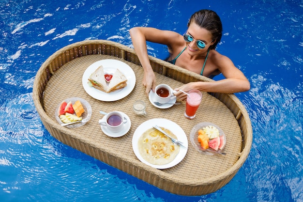 Férias no resort. Jovem mulher feliz com um café da manhã flutuante na piscina.