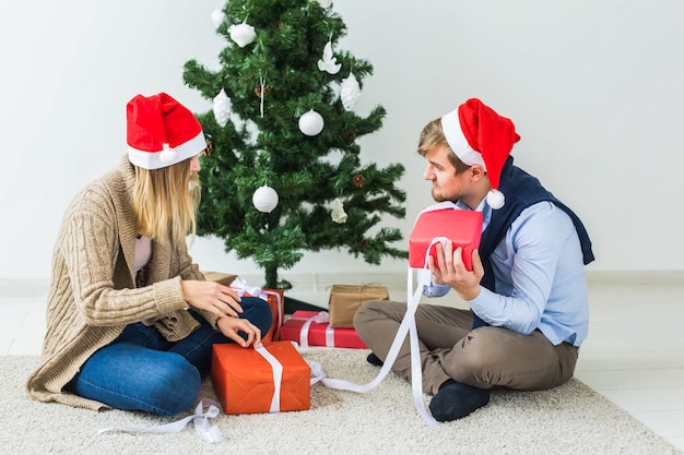 Férias, relacionamento e conceito festivo - casal abrindo presentes juntos perto da árvore de Natal.