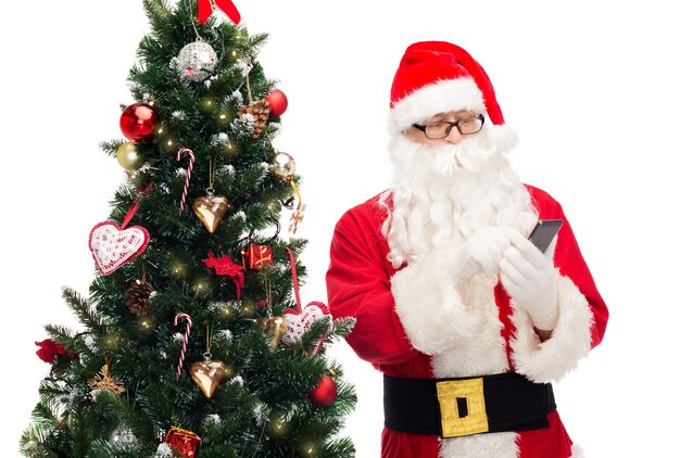 férias, tecnologia e conceito de pessoas - homem fantasiado de papai noel com smartphone e árvore de natal