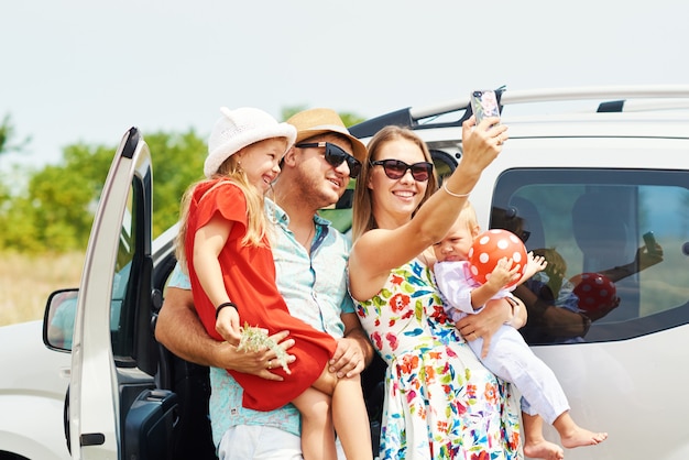 Foto férias, viagens - família feliz e pronta para a viagem para as férias de verão. as pessoas se divertem e tiram fotos no telefone. tire uma selfie na memória da viagem