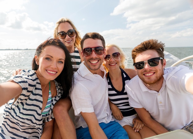 Férias, viagens, mar, amizade e conceito de pessoas - amigos sorridentes sentados no convés do iate e fazendo selfie