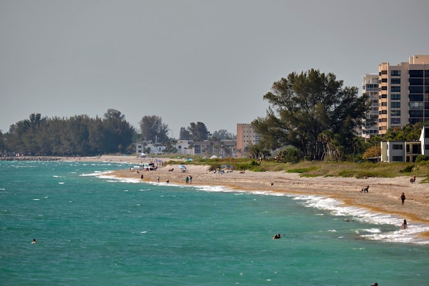 Ferienortstrand mit weißem Sand, blauem Wasser, hohen Hotelgebäuden, glückliche Menschen, die sich sonnen und im Meer schwimmen.