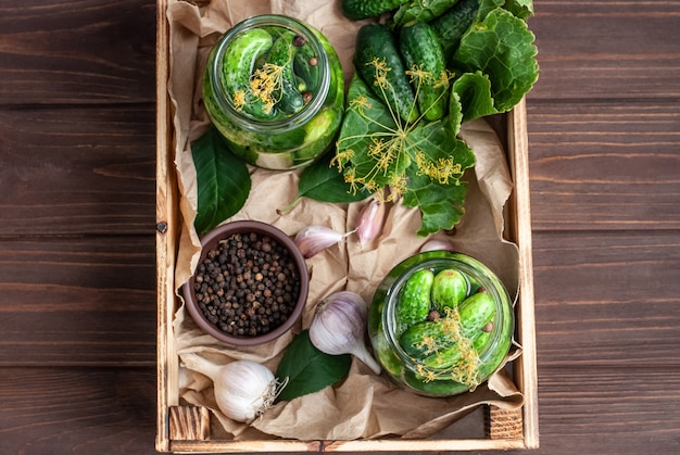 Fermentación de pepinos en frascos de vidrio. Pepinos crudos, flores de eneldo, hojas de cerezo, hojas de rábano picante, especias y hierbas en una bandeja