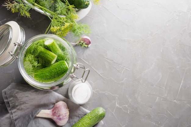 Fermentationsgurke im Glasgefäß mit Dill und Knoblauch auf grauer Tabelle