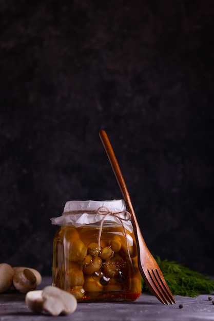 Fermentierte Champignon-Pilze in Dosen in einem Glas mit Knoblauch, Lorbeerblatt und Dill mit einer Holzgabel in einem zurückhaltenden Zustand