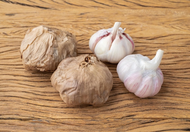 Fermentierter schwarzer Knoblauch und normale Knoblauchzwiebeln über Holztisch