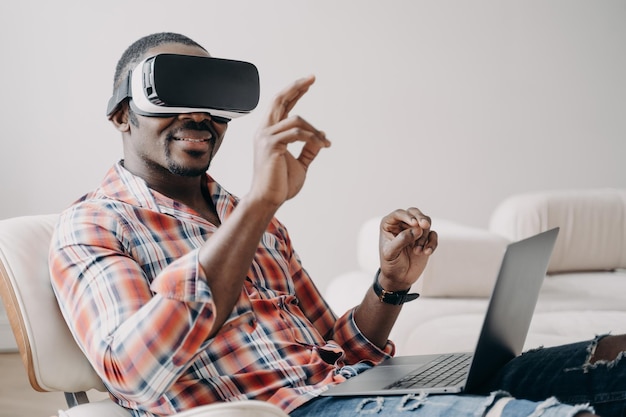Fernarbeit und futuristisches Gaming Afroamerikaner in vr-Brille, der zu Hause mit Laptop arbeitet
