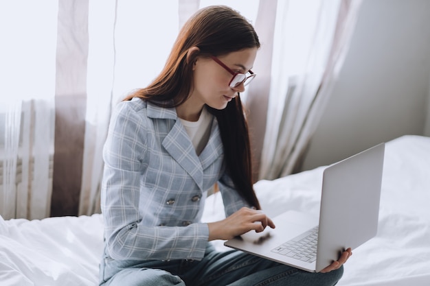 Fernarbeit zu Hause, Frau auf der Couch, die mit einem Laptop arbeitet und auf den Bildschirm schaut