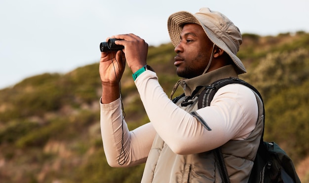 Fernglaswandern oder schwarzer Mann auf einem Berg in der Natur auf einer Trekkingreise oder einem Abenteuer für die Freiheit. Sehen Sie sich Urlaubsferien an oder gehen Sie als afrikanischer Wanderer spazieren, um im Park nach körperlicher Betätigung, Fitness oder Wellness zu suchen
