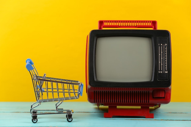 Fernseher Supermarkt. Einkaufswagen mit Retro-Fernseher auf gelbem Hintergrund