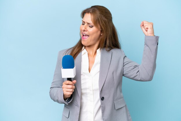 Fernsehmoderatorin mittleren Alters über isoliertem blauem Hintergrund, die einen Sieg feiert