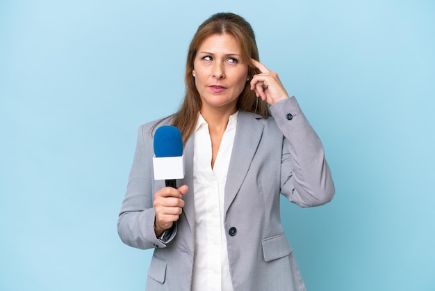 Fernsehmoderatorin mittleren Alters über isoliertem blauem Hintergrund, die Zweifel hat und nachdenkt