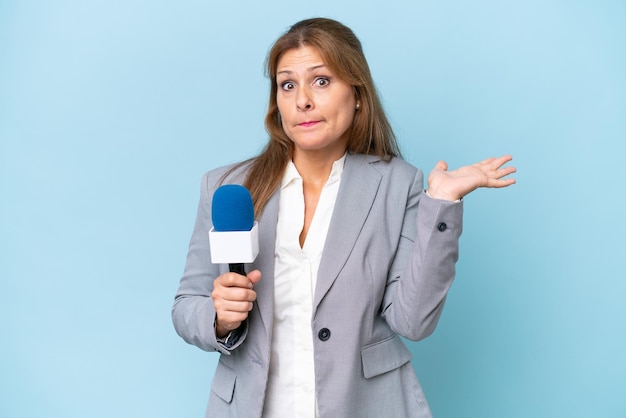 Fernsehmoderatorin mittleren Alters über isoliertem blauem Hintergrund, die Zweifel hat, während sie die Hände hebt