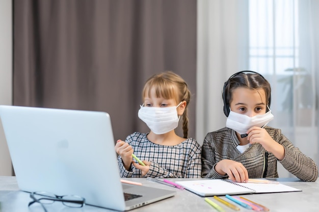 Fernunterricht. Schulmädchen am Laptop mit Maske online lernen Zu Hause am Tisch sitzen