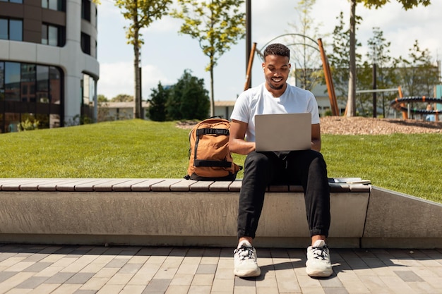 Fernunterrichtskonzept Schwarzer männlicher Student mit Laptop, der im Freien sitzt und sich ein Bildungs-Webinar ansieht