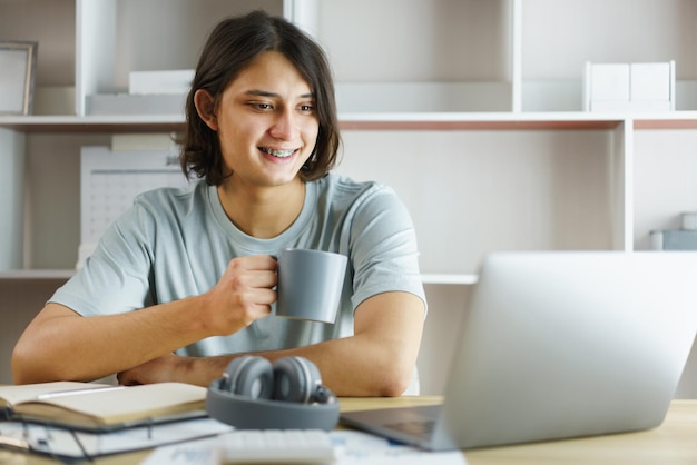 Fernunterrichtskonzept teenie-junge trinkt kaffee und lernt unterrichtsstunde online zu hause