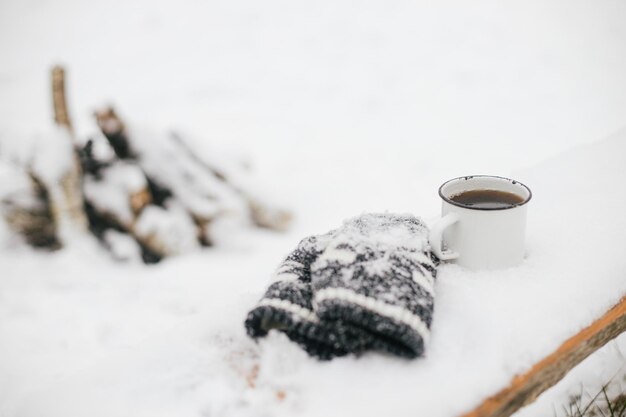 Fernweh Warme Tasse Tee und kuschelige Strickhandschuhe im Schnee auf Holzbank im Winterpark Wandern