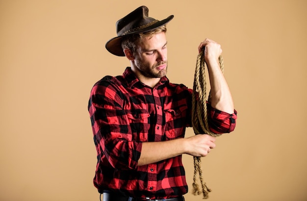 Ferramenta de laço do cowboy americano Vida ocidental Homem cowboy fundo bege Homem usando chapéu segurando corda Ocupações de rancho O laço é usado em eventos competitivos de rodeios O laço pode ser amarrado ou embrulhado