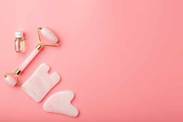 Ferramenta de massagem Gua sha feita de rolo de quartzo rosa natural, pedra jade e óleo, sobre um fundo rosa para cuidados com o rosto e o corpo. Parte da medicina tradicional chinesa