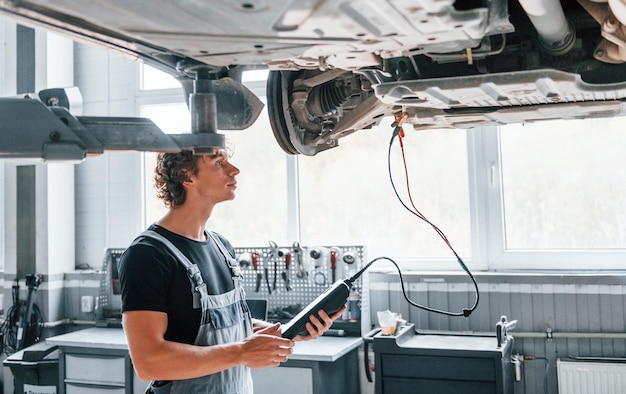 Ferramenta especial para testar características Homem adulto de uniforme cinza trabalha no salão de automóveis