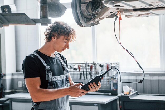 Ferramenta especial para testar características homem adulto de uniforme cinza trabalha no salão de automóveis