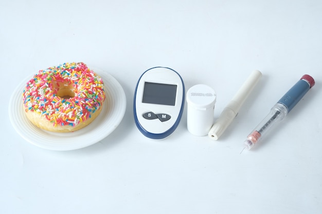 Ferramentas de medição de diabéticos, insulina e donuts em fundo branco