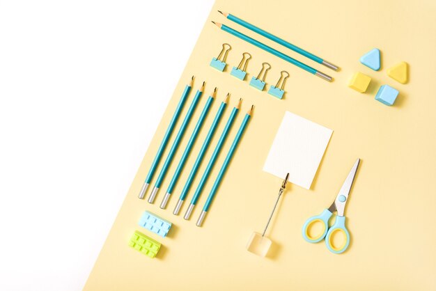 Ferramentas escolares em fundo azul e amarelo. vista superior knolling.back to school, material escolar - lápis e tintas, régua e borracha, clipes de papel e tesouras, blocos de notas e cadernos.