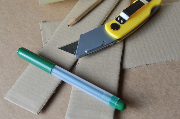 Ferramentas para trabalhar com papelão dispostas sobre uma mesa com restos de papelão.