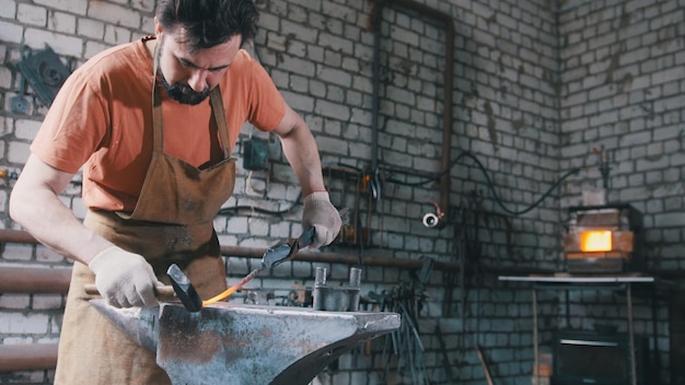Ferreiro com martelo na forja criando faca de aço, pequeno negócio