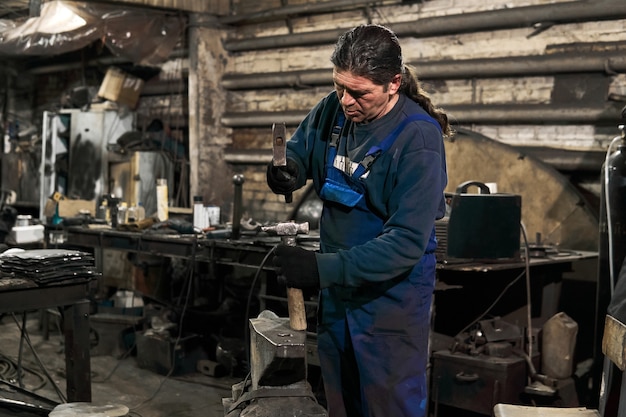 Ferreiro idoso endireita um martelo em uma oficina se preparando para o trabalho