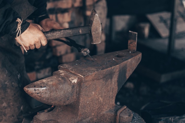 Ferreiro trabalhando metal com martelo e pinças na bigorna na forja Ferro de ataque do ferrador na oficina Metalurgia