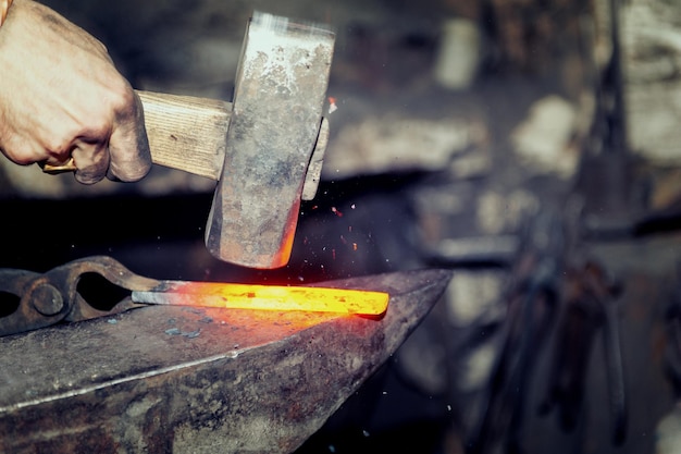 Ferreiro trabalhando metal com martelo na bigorna na forja