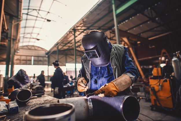 Ferro de solda do trabalhador. Traje de proteção e máscara. Interior da oficina.