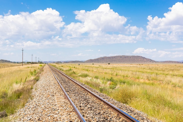 Ferrocarril en medio de un campo de hierba seca bajo el nublado cielo azul